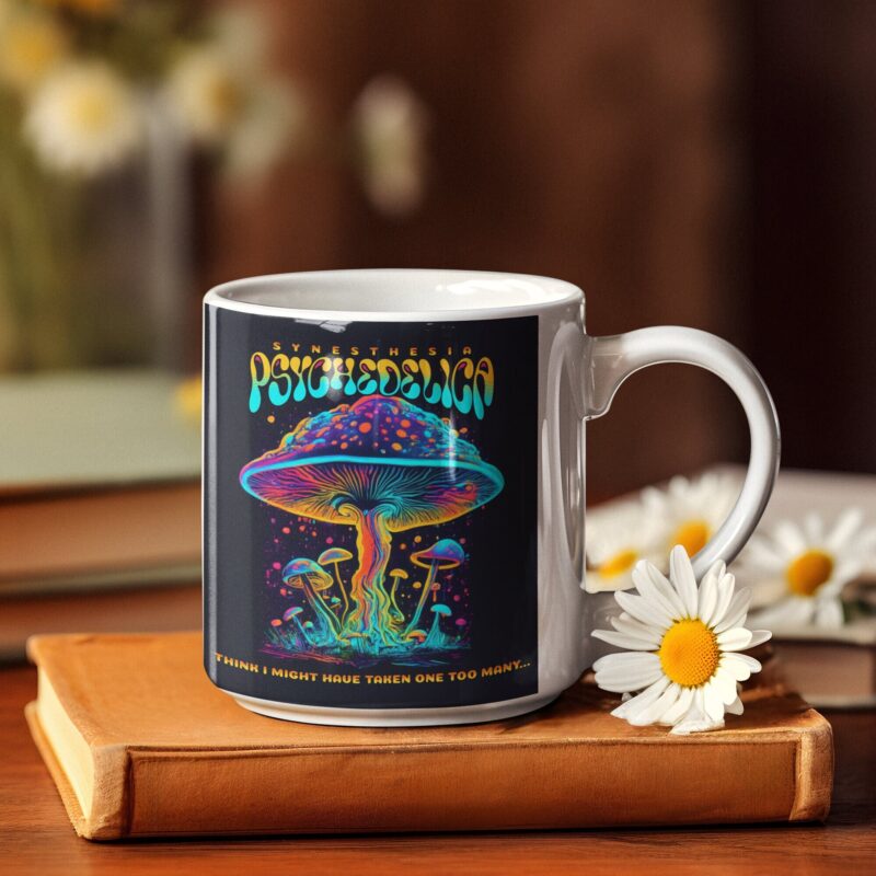White mug with a vibrant psychedelic mushroom design, sitting on a book with daisies in the background.