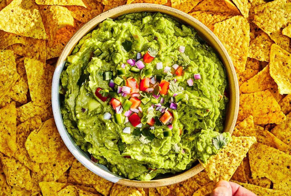 Fresh guacamole dip made with avocado, lime, onion, and cilantro served in a bowl with tortilla chips